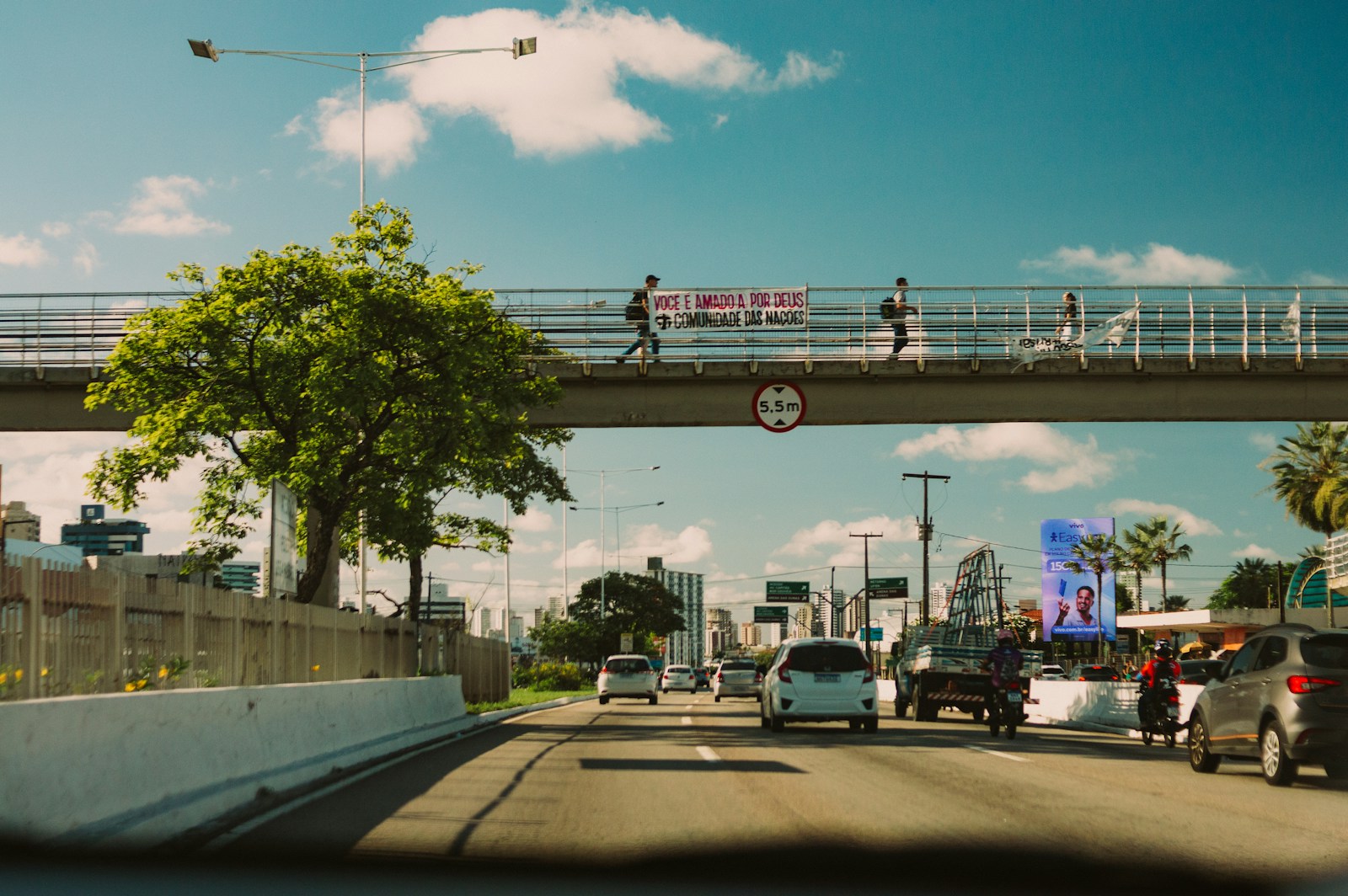 Pessoas atravessando uma passarela sobre uma via urbana movimentada