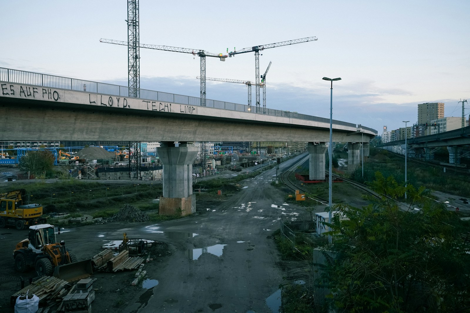 Obra de infraestrutura com guindastes, máquinas e uma ponte