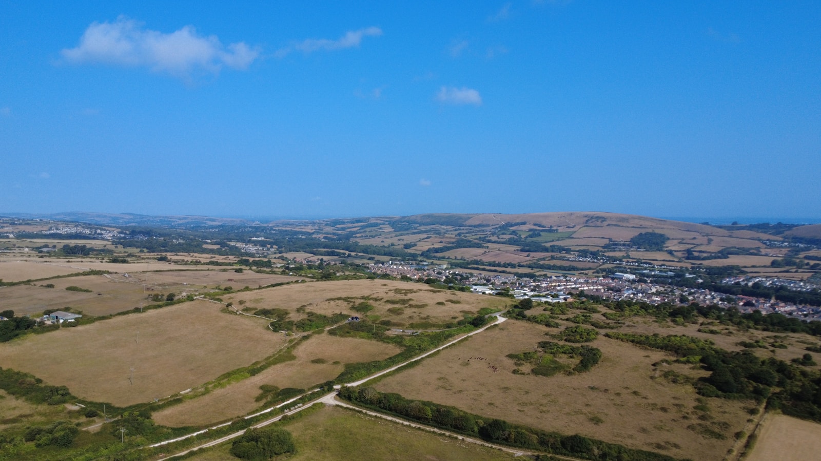 Paisagem rural com campos, colinas e uma pequena cidade ao fundo